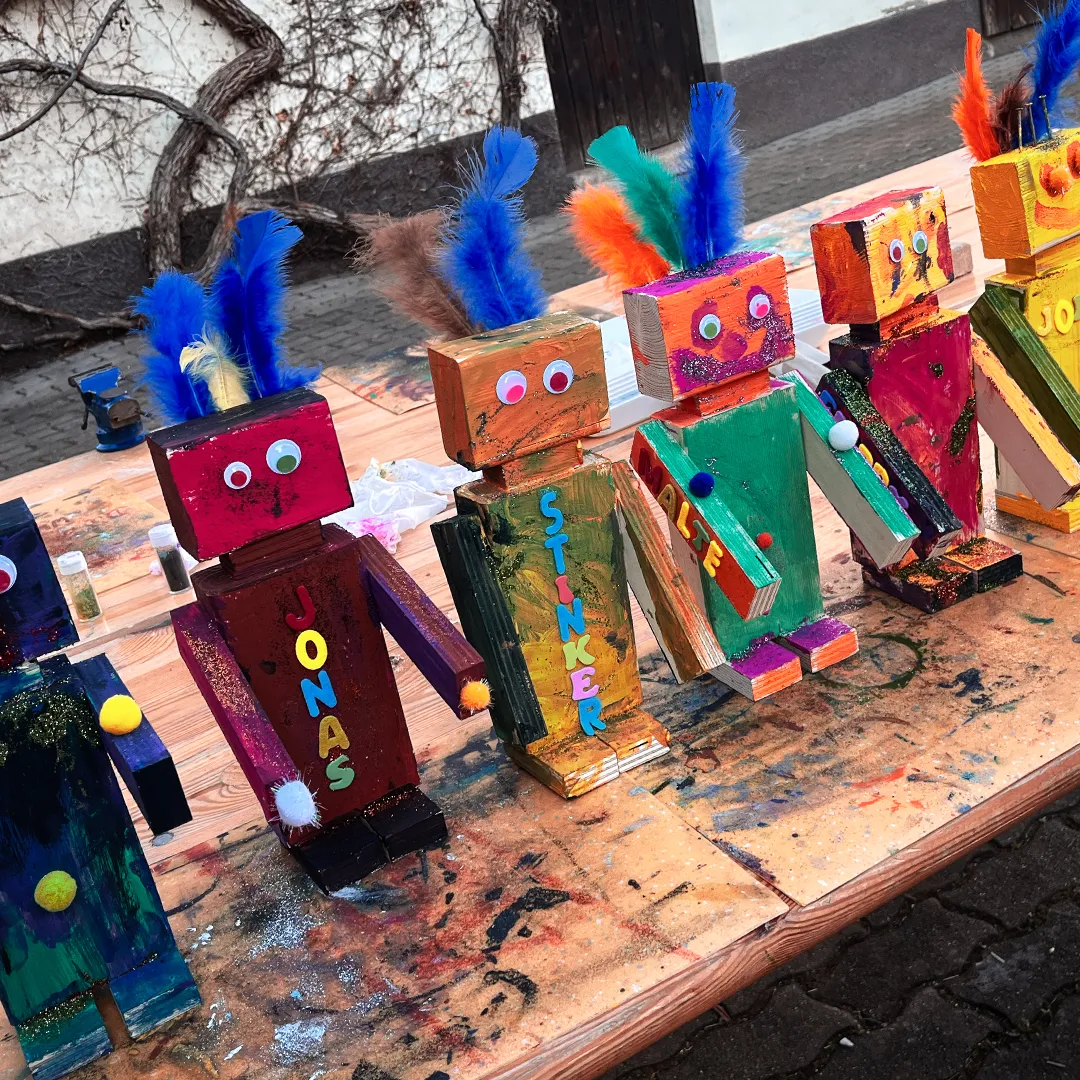 aus holz gebastelte und bemalte roboter lustig mit dem jeweiligen namen des kindes aus ausgeschnittenen buchstaben aufgeklebt