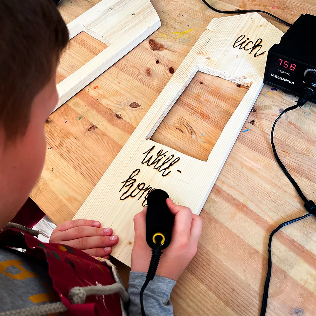 ein junge graviert mit einen loetkolben die worte herzlich willkommen in ein stueck holz
