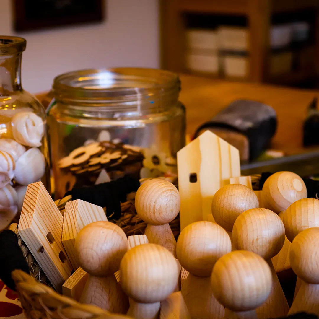im vordergrund holzfiguren zum basteln im holzkorb dahinter zwei offene glaeser mit muscheln und holzblumen