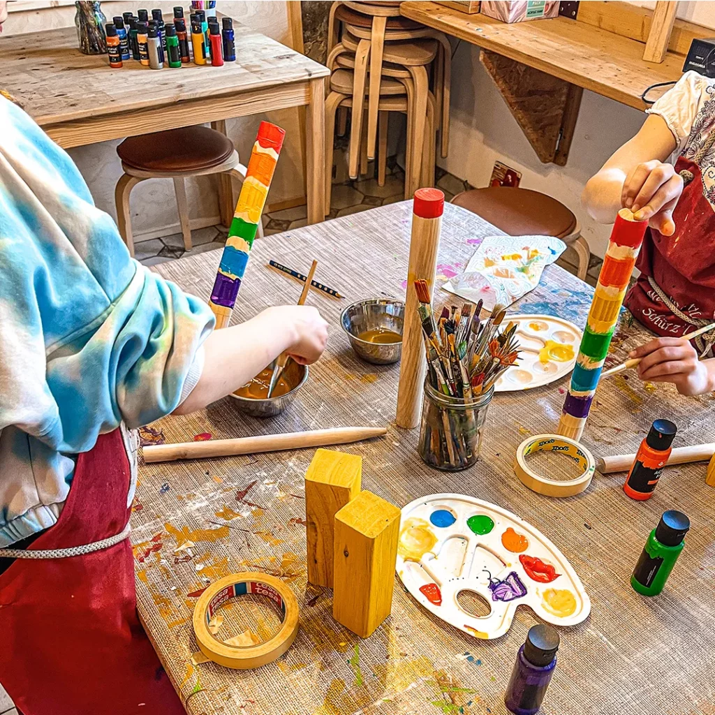 kinder bemalen holzstaebe die sie zuvor zugeschnitten haben