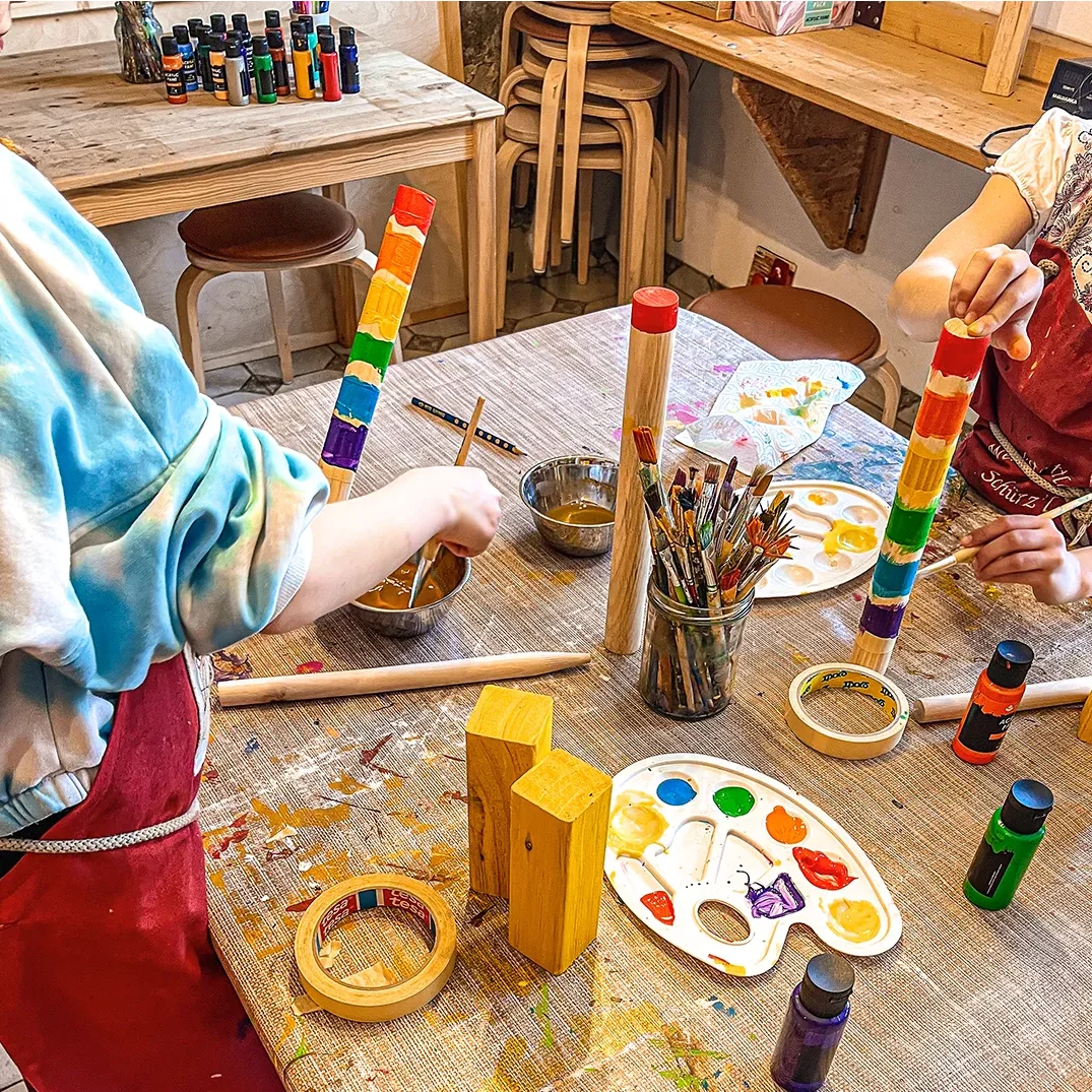 kinder bemalen holzstaebe die sie zuvor zugeschnitten haben