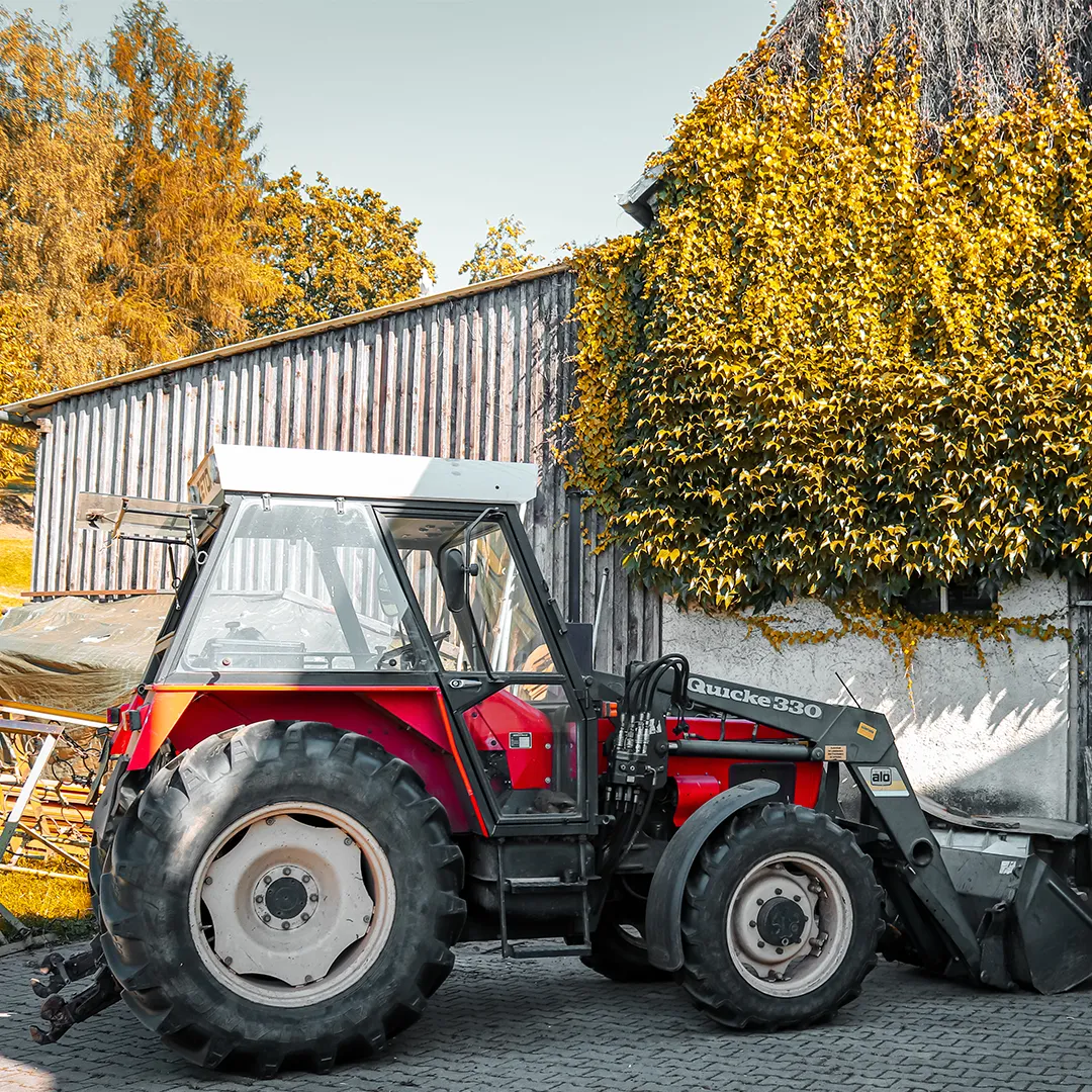 roter traktor mit schaufel von der seite im hintergrund mit bewachsener scheunen wand